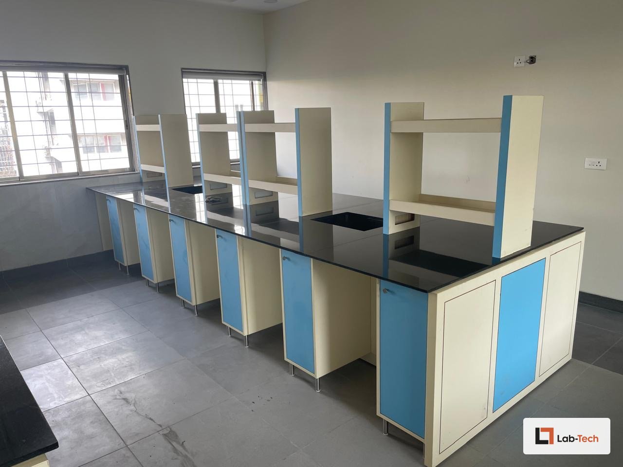 Installed Lab-Tech island bench with a black granite worktop and reagent shelving, in a daylight lab.
